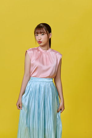 Portrait of a cheerful young girl in dress looking at camera isolated over yellow backgroundの写真素材
