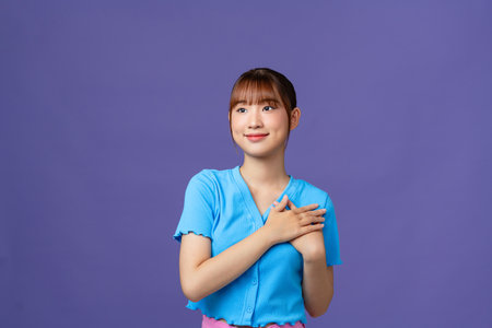 Happy pleased pretty young woman holding hands on chest feeling gratitude, standing isolated at white backgroundの写真素材