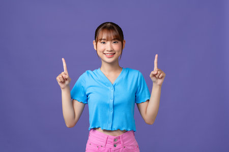 Young Asian woman showing and pointing up with fingers, inviting use link isolated purple backgroundの写真素材