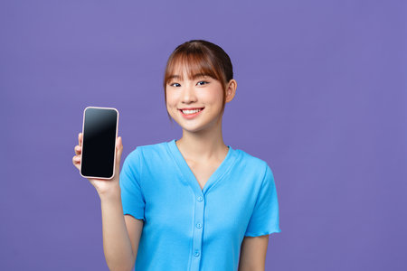 Portrait of a smiling young woman showing smartphone screen isolated on a violet backgroundの写真素材