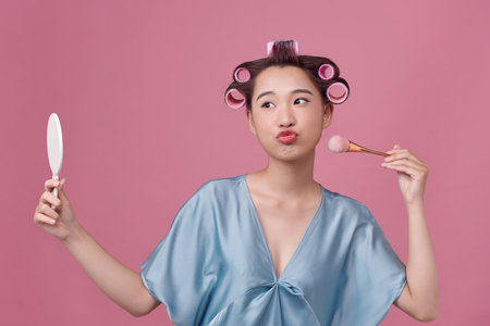 Portrait of happy asian woman with lotion spray and curlers in her hairの写真素材