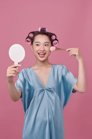 Pretty woman with curlers on hair, holding makeup brushes and mirror in handsの写真素材