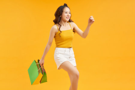 Attractive dreamy cheerful girl holding in hand carrying new things isolated on yellow backgroundの写真素材