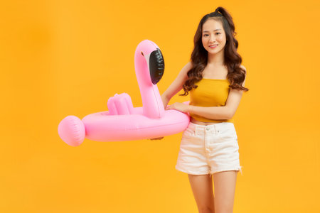 A young woman holds an inflatable flamingo over yellowの写真素材
