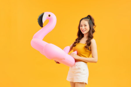 Smiling young woman with an inflatable flamingo isolated on vivid yellow backgroundの写真素材