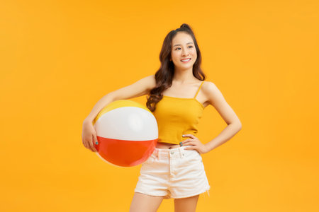 Young asian woman holding beach ball isolated on vivid yellow background happyの写真素材