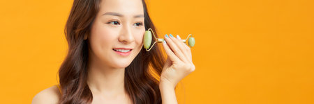 Beautiful young Asian woman using jade face roller, massager the skin of the faceの写真素材