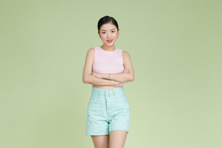Smiling woman with arms crossed standing against pastel green backgroundの写真素材