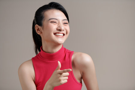 young smiling positive asian happy woman stand point index finger aside on workspace copy spaceの写真素材