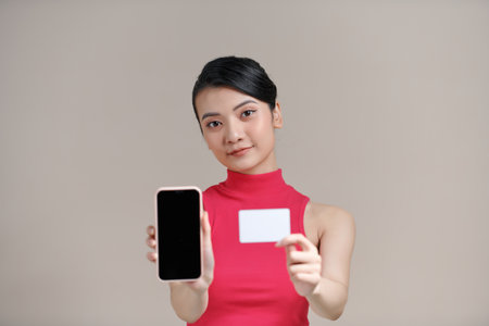 Photo of pleased young woman posing isolated,  using mobile phone holding debit card.の写真素材