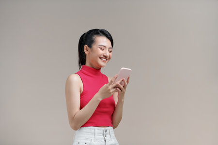 Asian woman smile standing playing game or writing SMS message on smartphone looking to the phoneの写真素材