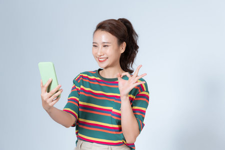 Good-looking young woman with smartphone showing OK sign.の写真素材