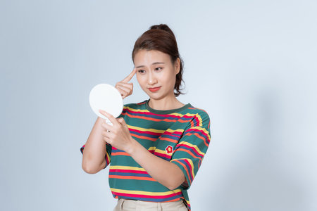 young woman tightens her eyes and eyebrows in the mirrorの写真素材