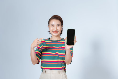 Beautiful Asian woman smile holding a smartphone on hand and pointing finger to the blank screenの写真素材