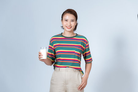 Happy young Asian woman drinking milk from the glass over white background, shake looking at cameraの写真素材