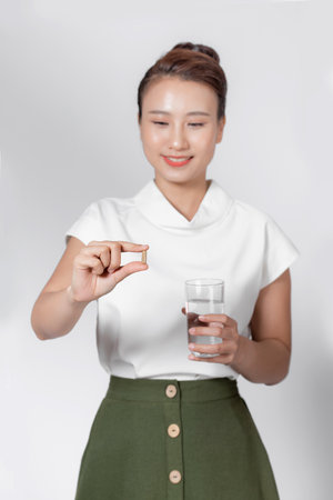 Beautiful smiling woman taking vitamin pill and holding glass of fresh water in morning.の写真素材