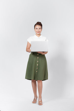 Photo of asian woman standing and holding laptop isolated over white backgroundの写真素材