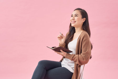 Thoughtful young vietnamese woman thinking about something and holding notebook isolatedの写真素材