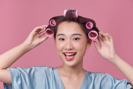 Cheerful asian girl with hair curlers rollers by hairdresser.の写真素材