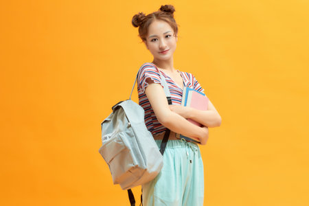Young happy student with backpack on yellow backgroundの写真素材