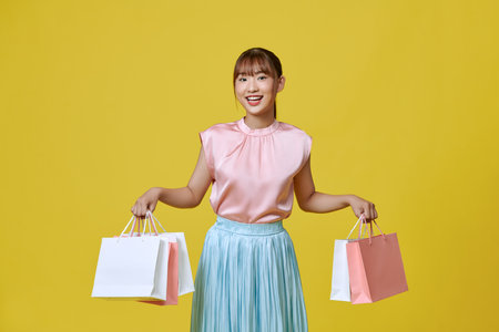 beautiful girl in elegant spring dress holding shopping bags on yellow backgroundの写真素材