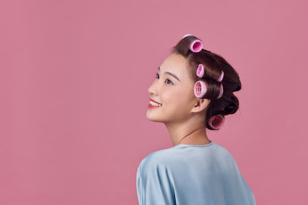 Young woman is daydreaming while wearing hair rollers, isolated over whiteの写真素材