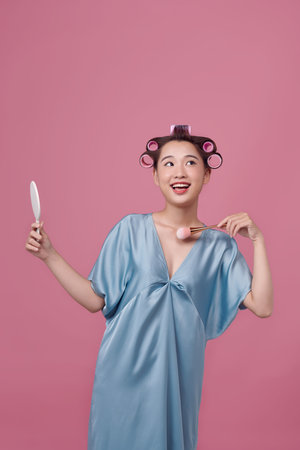 Cute girl with hair curlers doing makeup on her face at the makeup table, using makeup brushの写真素材