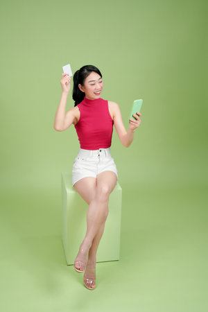 Smiling woman sitting on podium showing credit card and holding smartphone in another handの写真素材