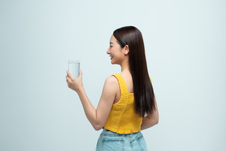 Back view of smiling asian woman holding glass of water, healthy living conceptの写真素材