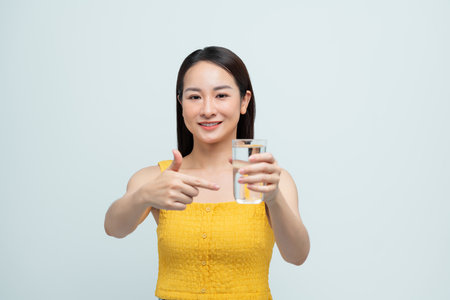 Smiling Woman Holding Glass of Water Indoors on Light Backgroundの写真素材