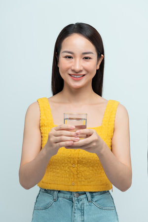 A smiling woman holding a glass water. Promoting hydration, health, and eco-friendly living.の写真素材