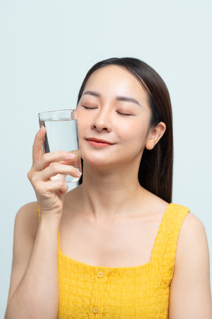asian woman smile drinks a glass water happily in a white roomの写真素材