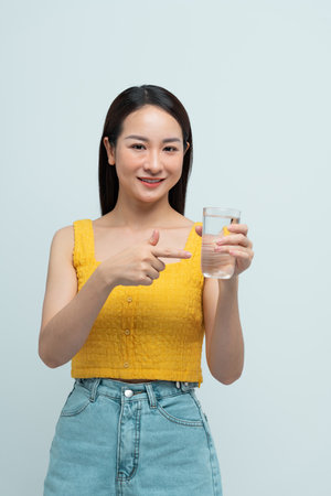 Young beautiful woman drinking glass of water smiling happy pointing with hand and fingerの写真素材