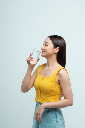 Cheerful woman drinking water from glass standing over white backgroundの写真素材