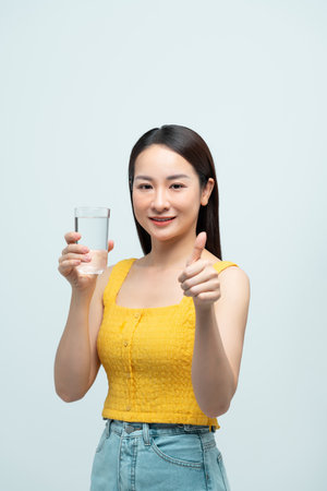 Cheerful woman holding a glass of water and giving a thumbs up gestureの写真素材