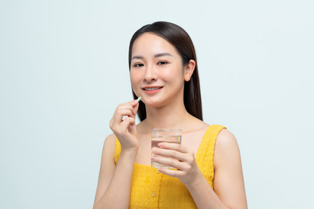 Beautiful young woman taking pills on white backgroundの写真素材
