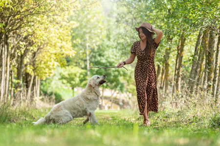Young woman playing with her white dog on a path between treesの写真素材