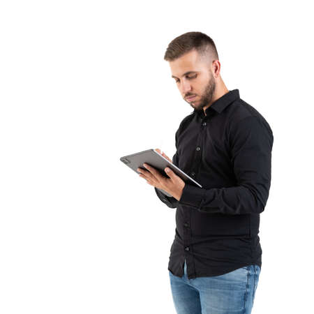 Young man with a black shirt looking a a grey tablet on a white backgroundの写真素材