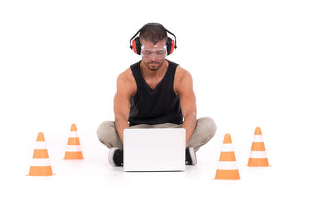 Constructor man working with a laptop within a delimited area with orange cones