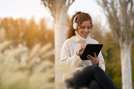 Young woman writing with on a tablet and listening to music in the parkの写真素材