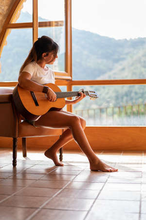 Singing woman playing Spanish guitar next to a window.の写真素材