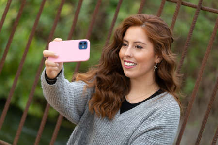 Young redhead woman taking a selfie sitting in the park with a big smile