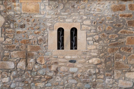 Old stone wall with a double arched window and metal grating