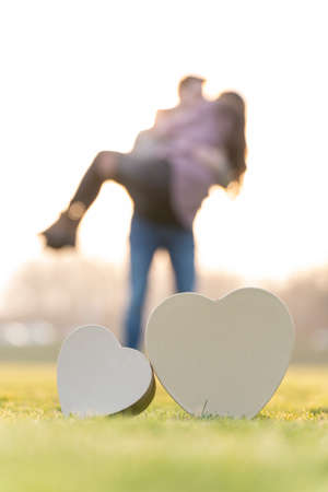 Young couple hugging behind two heart shapes in a park on valentines dayの写真素材