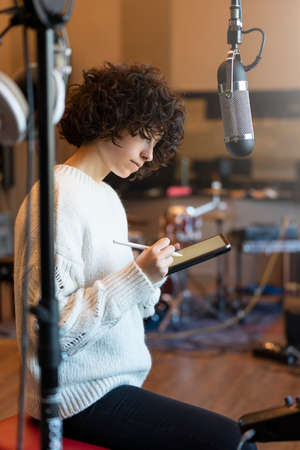 Young woman with curly hair sitting and thinking what to write in the music studioの写真素材