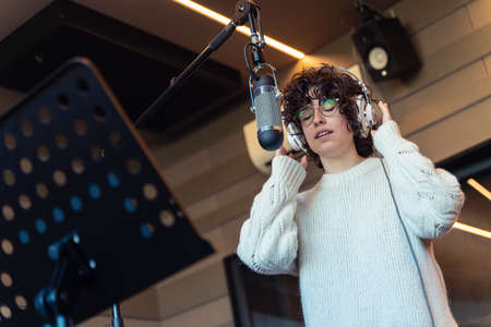 A young curly hair singer woman with glasses recording a song in a real studioの写真素材