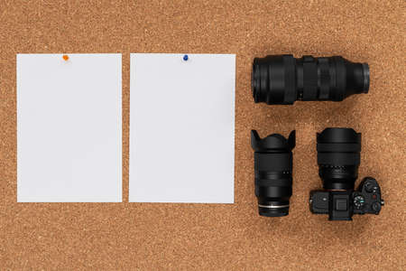 Cork board with photo camera, two lenses and white paper hanging on a thumbtack