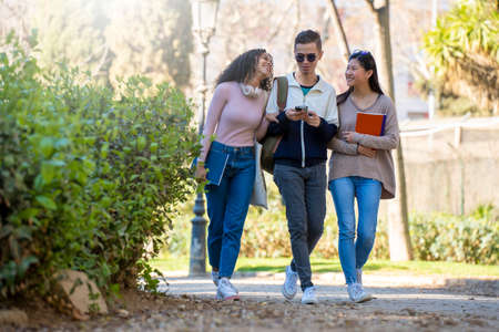 Three young multiethnic students walking in the street and looking at the phone