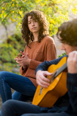 Young curly woman singing with a guitarist man in the street