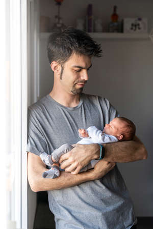 Young father with her newborn baby in her arms at home near the window